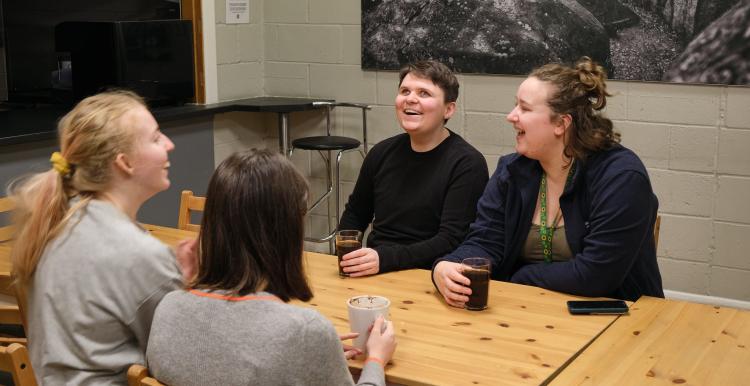 four women sit around a table and are laughing