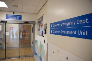 Hallway inside a hospital with a blue sign pointing to the Children's emergency department