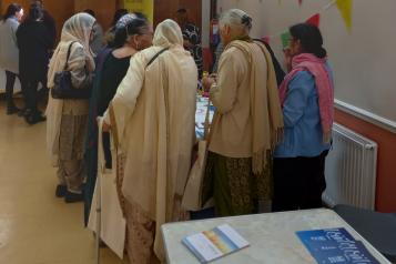 a group of women huddle round a table to read some information leaflets.