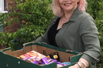 a woman holds a box of assorted food items.