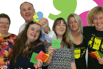 A group of people smile at the camera whole holding post-it notes with thumbs up drawn on them.