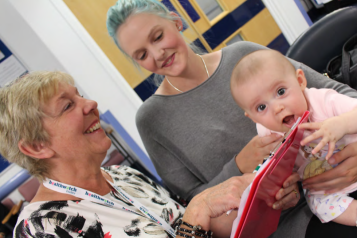 A Healthwatch Dudley volunteer talks to a woman and her baby in a waiting room