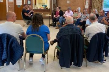 A group of people sit in a semi circle and are discussing.