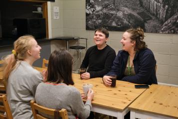 four women sit around a table and are laughing