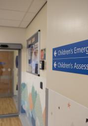 Hallway inside a hospital with a blue sign pointing to the Children's emergency department