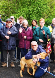 a group of people stand outside and wave at the camera. a dog is at the front of the group