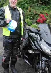 A man in a high visibility jacket stands next to a motorbike while holding a bag of prescription medication.